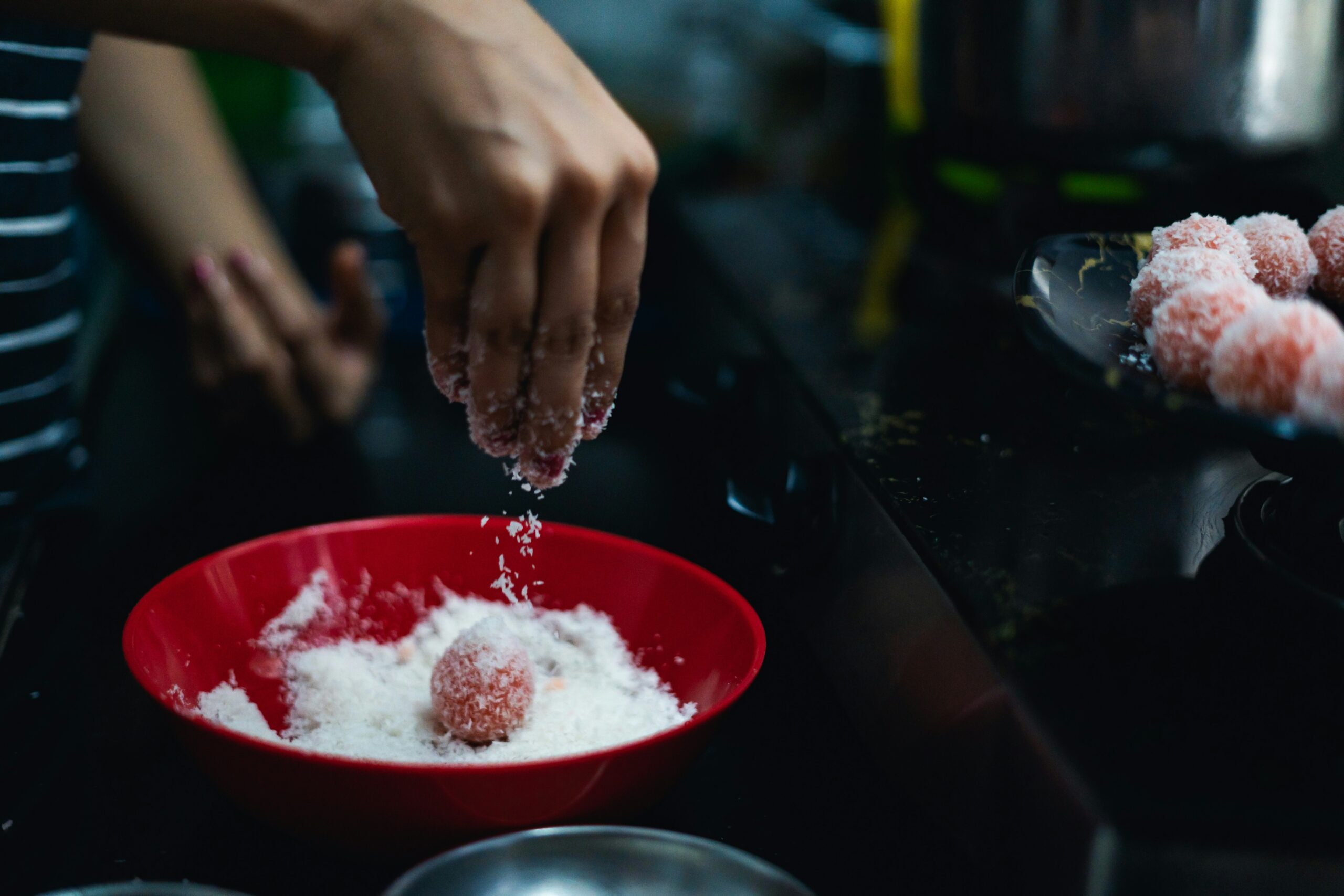A person is sprinkling sugar onto a bowl of doughnuts